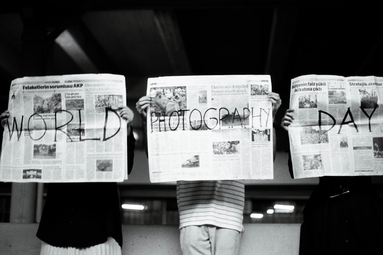 Three people hold newspapers with World Photography Day text, artistic vibe.