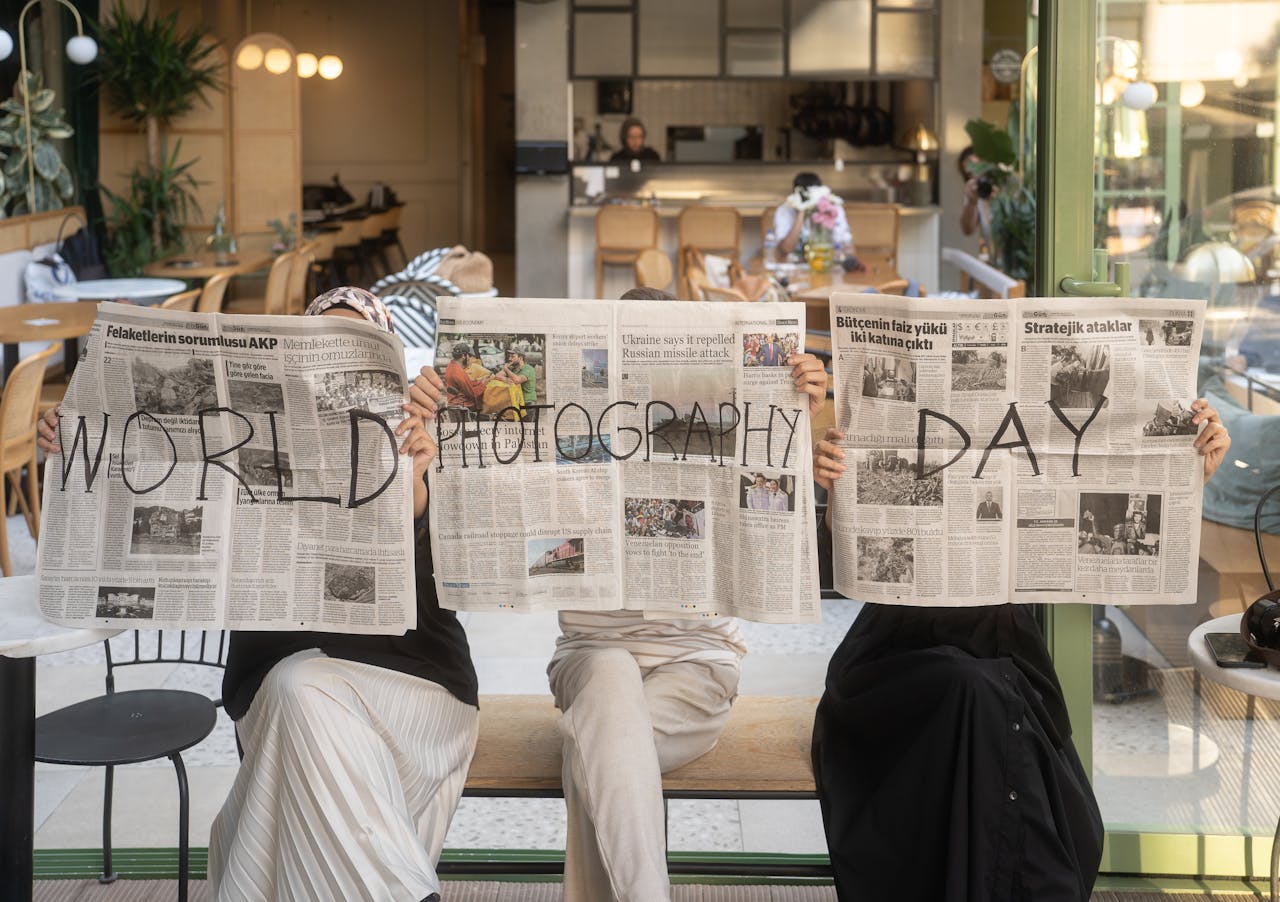Three people holding newspapers promoting World Photography Day in a cozy Ankara café.